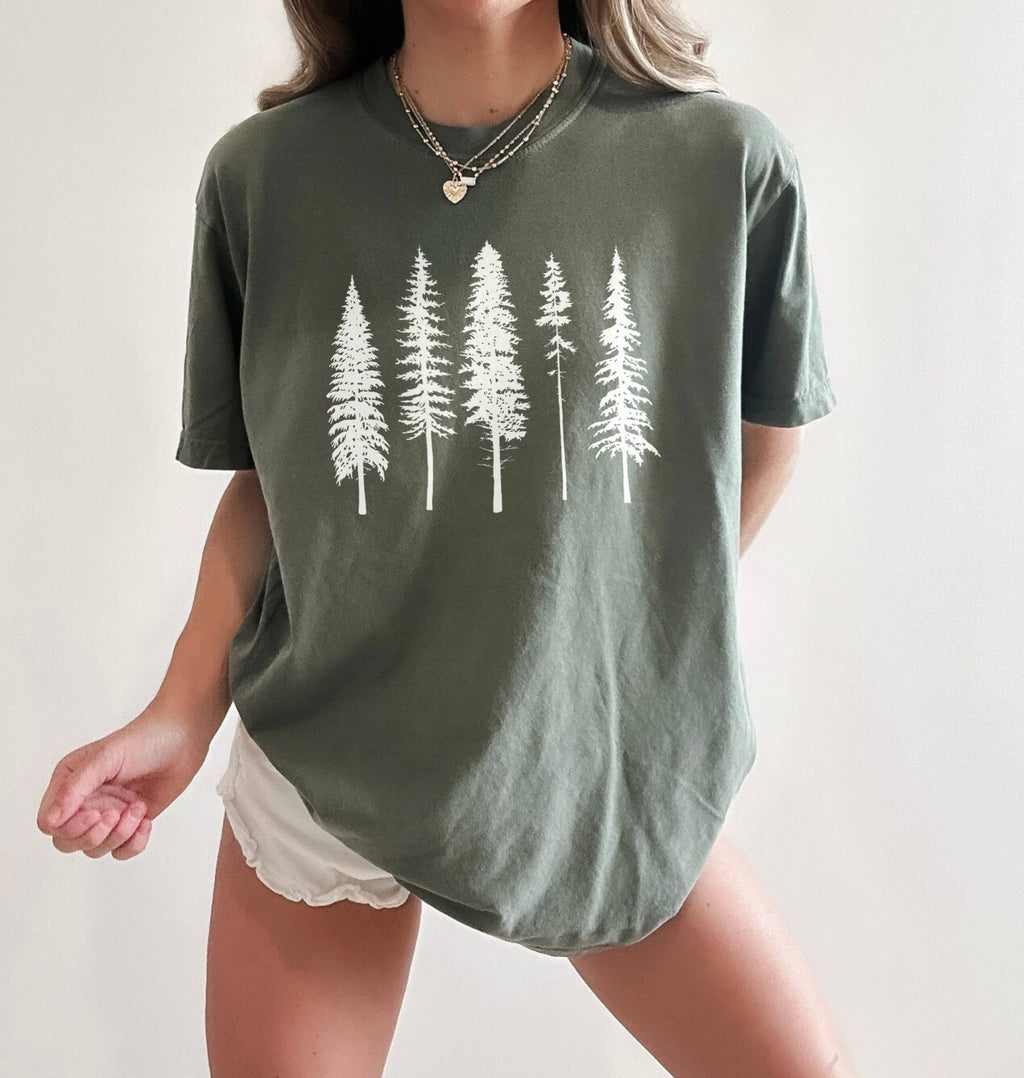 Person wearing sage  t-shirt with white pine tree forest graphic, minimalist nature design for hiking and outdoor lovers on a white background