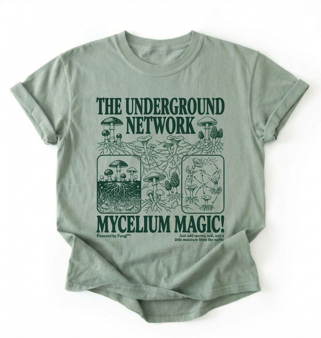 Flat lay of a sage green t-shirt featuring Mycelium network mushroom and root network illustrations with text reading “The Underground Network Mycelium Magic” with forest fungi design perfect gift for mushroom lovers nature fans and cottagecore style on a white background 