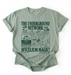 Flat lay of a sage green t-shirt featuring Mycelium network mushroom and root network illustrations with text reading “The Underground Network Mycelium Magic” with forest fungi design perfect gift for mushroom lovers nature fans and cottagecore style on a white background 