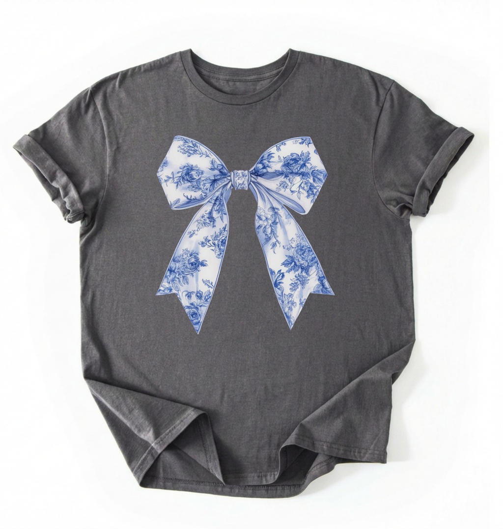 A charcoal heather t-shirt featuring a blue and white toile-patterned bow graphic printed on the chest, laid flat against a white background.