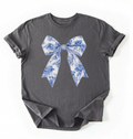 A charcoal heather t-shirt featuring a blue and white toile-patterned bow graphic printed on the chest, laid flat against a white background.
