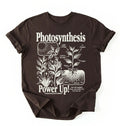Flat lay of a Espresso_Darkchocolate t-shirt featuring a botanical diagram with text reading “Photosynthesis Power Up.” for plant lovers and science fans perfect gardening gift for biology teachers and nature enthusiasts on a white background  