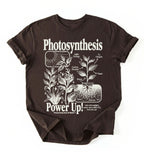 Flat lay of a Espresso_Darkchocolate t-shirt featuring a botanical diagram with text reading “Photosynthesis Power Up.” for plant lovers and science fans perfect gardening gift for biology teachers and nature enthusiasts on a white background  