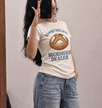 A woman takes a mirror selfie wearing a cream-colored graphic t-shirt with a sourdough bread illustration and the text 'SUPPORT YOUR LOCAL SOURDOUGH DEALER' in blue, paired with light-wash blue jeans.