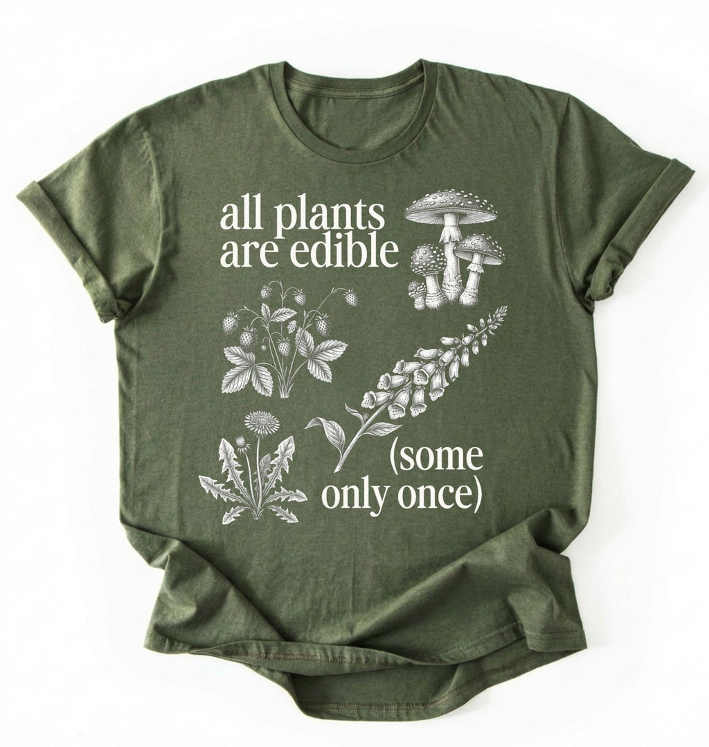 Flat lay of a Moss_MilitaryGreen shirt featuring botanical illustrations and text reading “All Plants Are Edible (Some Only Once).” with mushroom graphic for plant lover gardener gift cottagecore nature shirt on a white background 