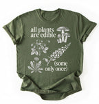Flat lay of a Moss_MilitaryGreen shirt featuring botanical illustrations and text reading “All Plants Are Edible (Some Only Once).” with mushroom graphic for plant lover gardener gift cottagecore nature shirt on a white background 