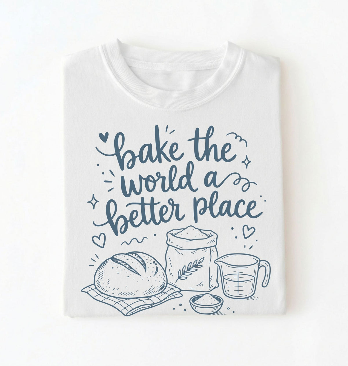 A folded white t-shirt with a navy blue graphic print that reads 'bake the world a better place' accompanied by illustrations of a loaf of bread, a bag of flour, a measuring cup, and a small bowl.
