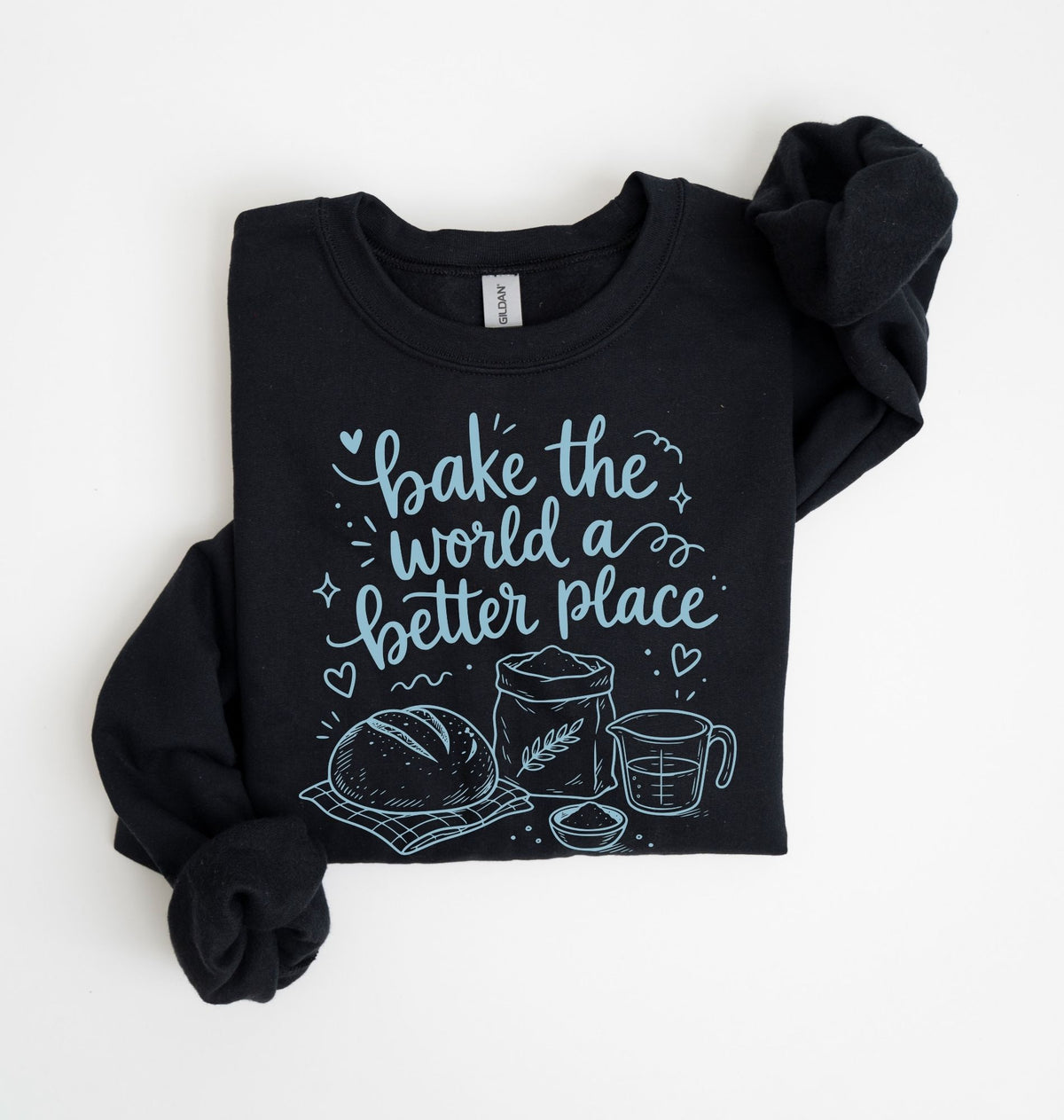 A black long-sleeve sweatshirt with rolled cuffs, featuring a light blue graphic print on the front that reads 'bake the world a better place' with illustrations of a loaf of bread, a wheat sack, and a measuring cup. The sweatshirt is laid flat on a white background.