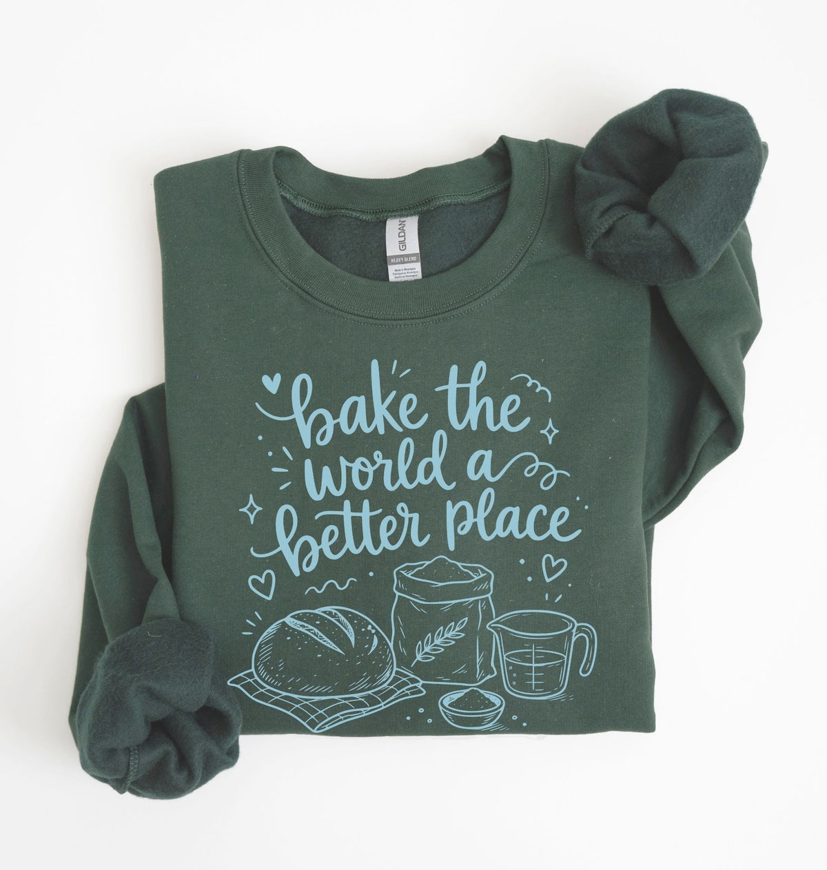 A forest green long-sleeve sweatshirt with rolled cuffs, featuring a light blue graphic print on the front that reads 'bake the world a better place' with illustrations of a loaf of bread, a wheat sack, and a measuring cup. The sweatshirt is laid flat on a white background.