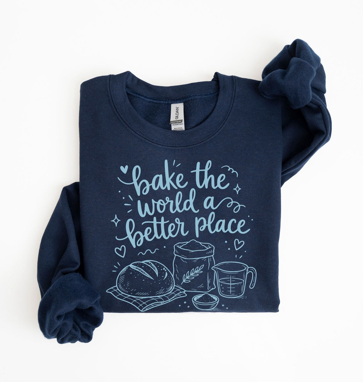 A navy blue long-sleeve crewneck sweatshirt with a light blue graphic print that reads 'bake the world a better place' accompanied by illustrations of a loaf of bread, flour sack, and measuring cup. The sweatshirt is neatly folded on a clean white background.