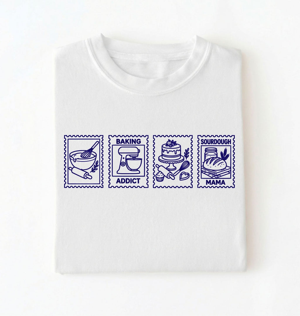 Flat lay of a white Baking Addict Sourdough Mama graphic shirt with vintage baking stamp design for bread bakers on a white background 
