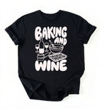 Flat lay of a black Baking and Wine graphic shirt for home bakers featuring baking tools and wine themed design on a white background