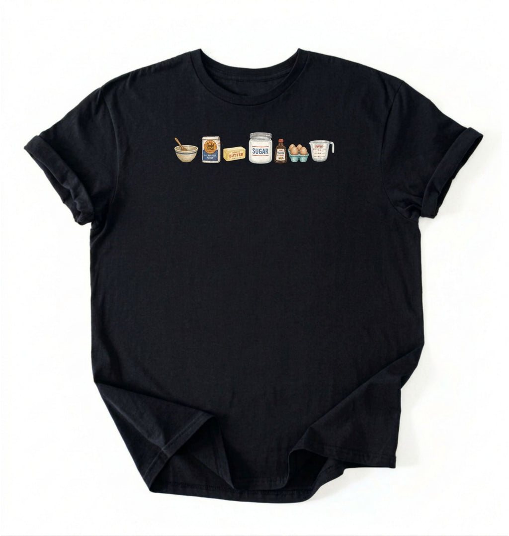 Flat lay of a black baking ingredients shirt with flour butter sugar eggs vanilla and measuring cup baker gift on a white background 