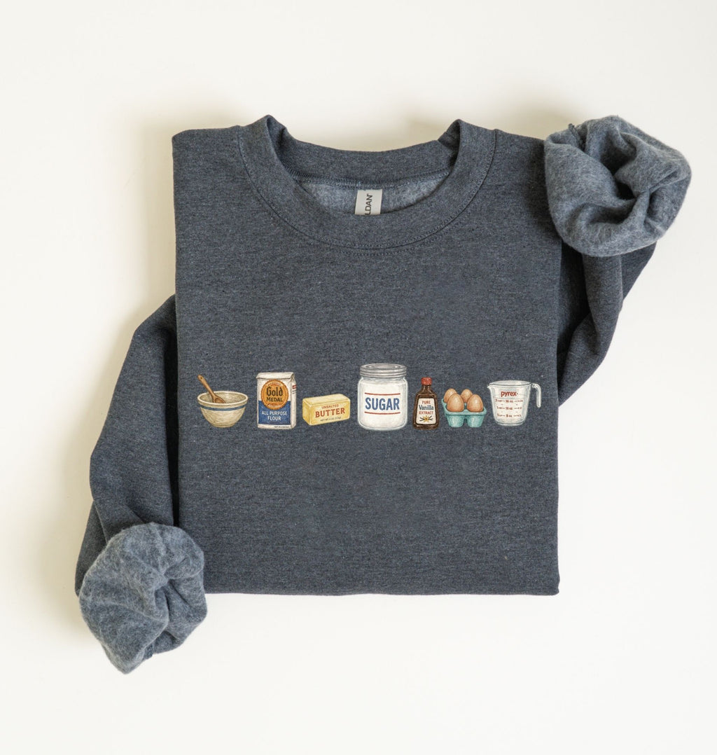 Flat lay of a dark heather baking ingredients sweatshirt with flour butter sugar eggs vanilla and baking essentials design on a white background