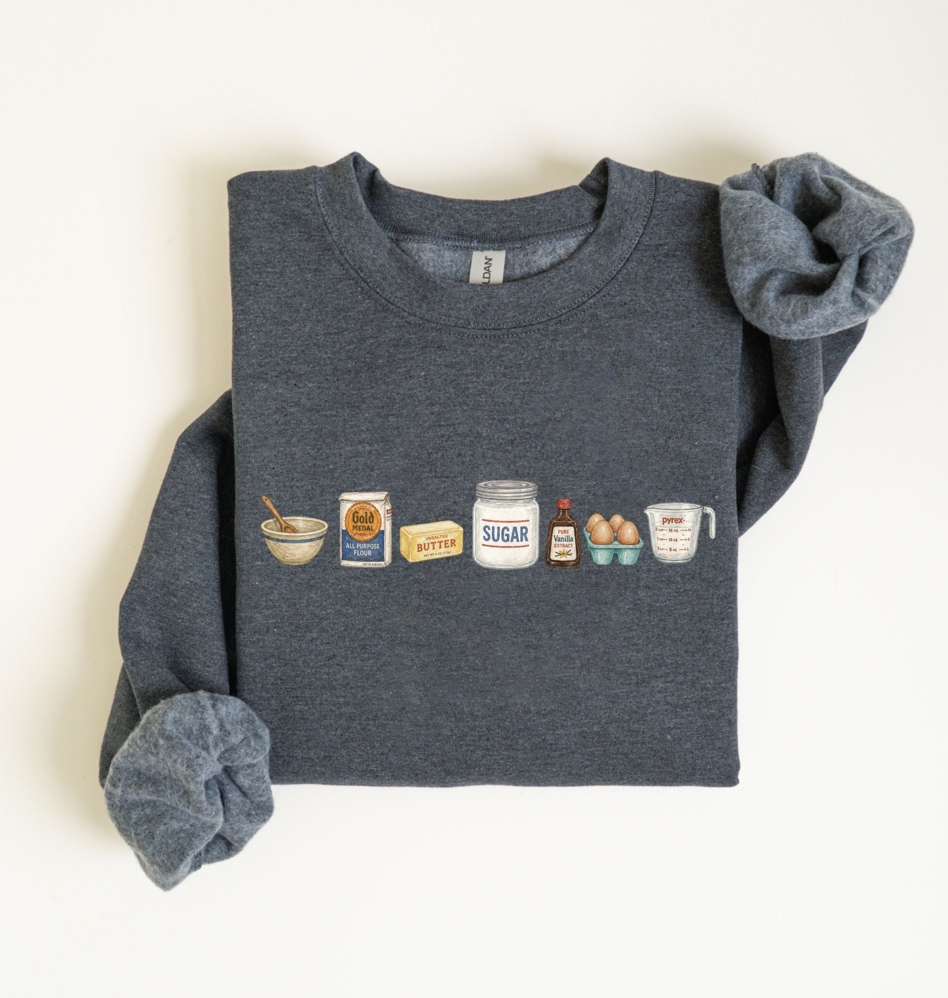 Flat lay of a dark heather baking ingredients sweatshirt with flour butter sugar eggs vanilla and baking essentials design on a white background