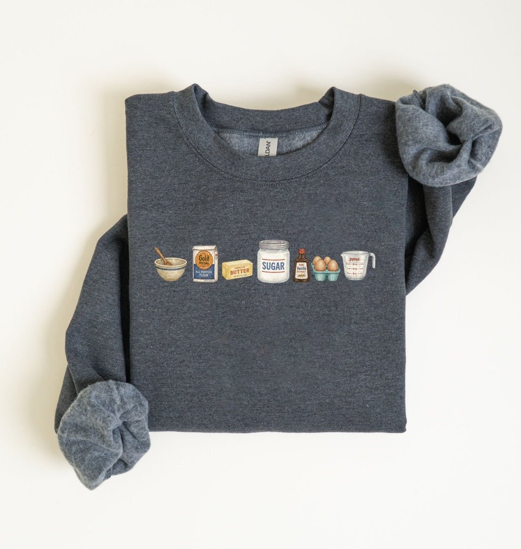Flat lay of a dark heather baking ingredients sweatshirt with flour butter sugar eggs vanilla and baking essentials design on a white background