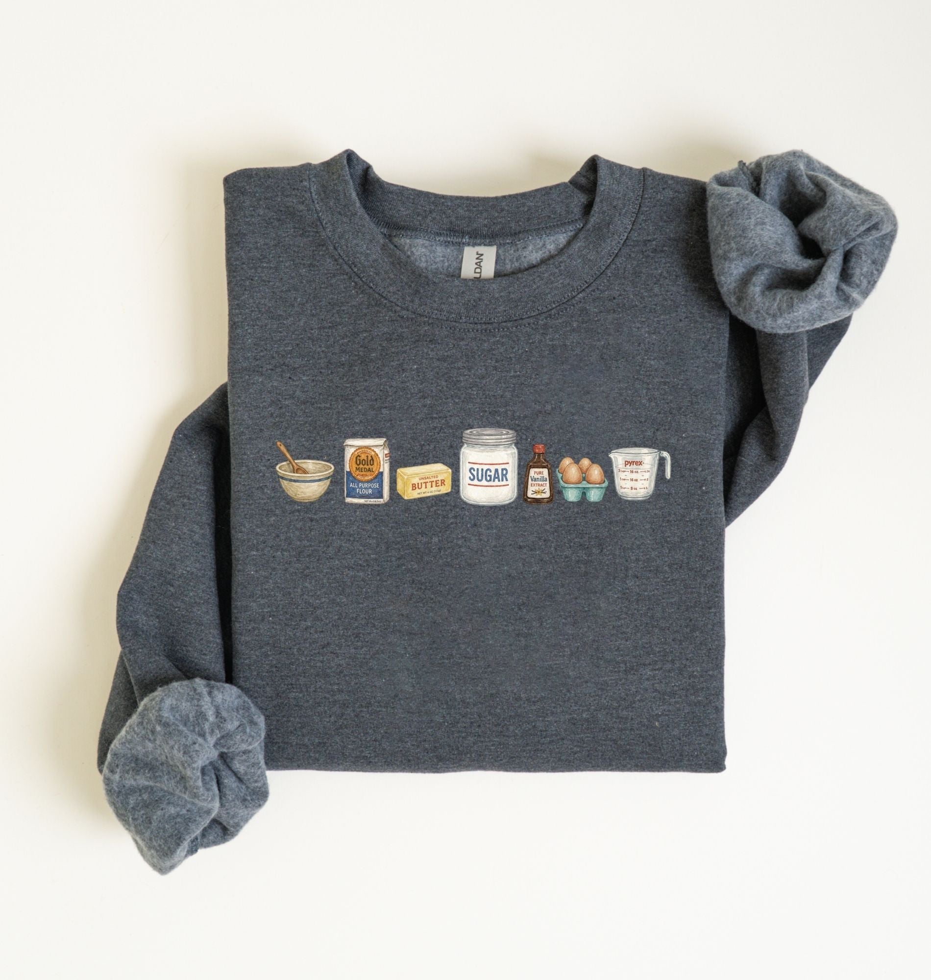 Flat lay of a dark heather baking ingredients sweatshirt with flour butter sugar eggs vanilla and baking essentials design on a white background
