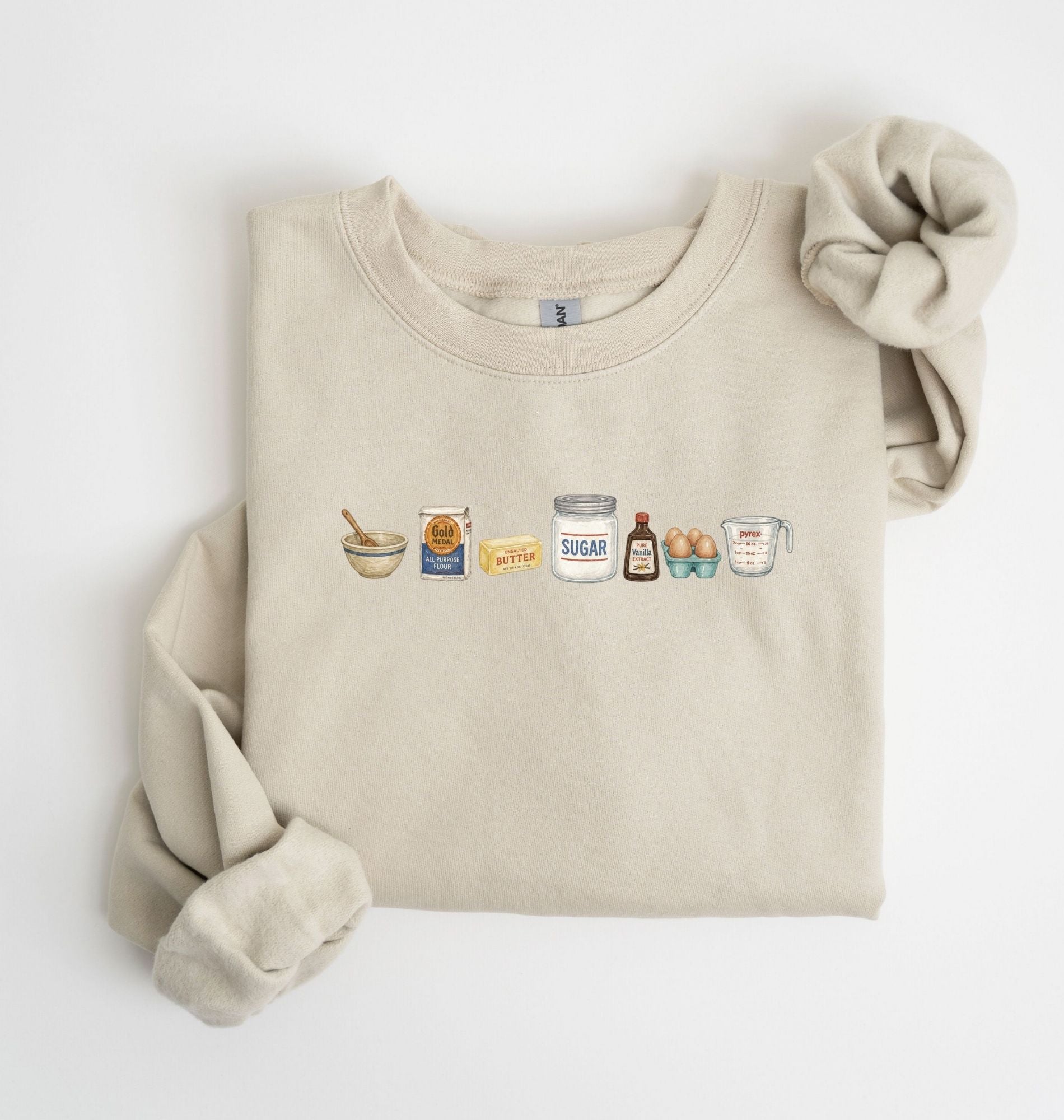 Flat lay of a sand baking ingredients sweatshirt with flour butter sugar eggs vanilla and baking essentials design on a white background