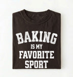 Flat lay of a brown Baking Is My Favorite Sport graphic shirt on navy blue t-shirt for home bakers on a white background 