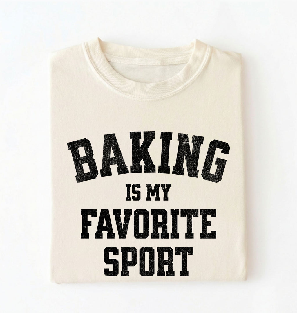 Flat lay of a cream Baking Is My Favorite Sport graphic shirt on navy blue t-shirt for home bakers on a white background 
