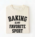 Flat lay of a cream Baking Is My Favorite Sport graphic shirt on navy blue t-shirt for home bakers on a white background 