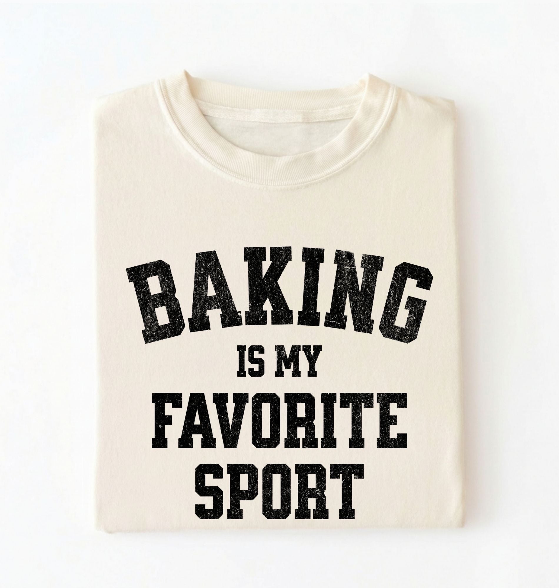 Flat lay of a cream Baking Is My Favorite Sport graphic shirt on navy blue t-shirt for home bakers on a white background 