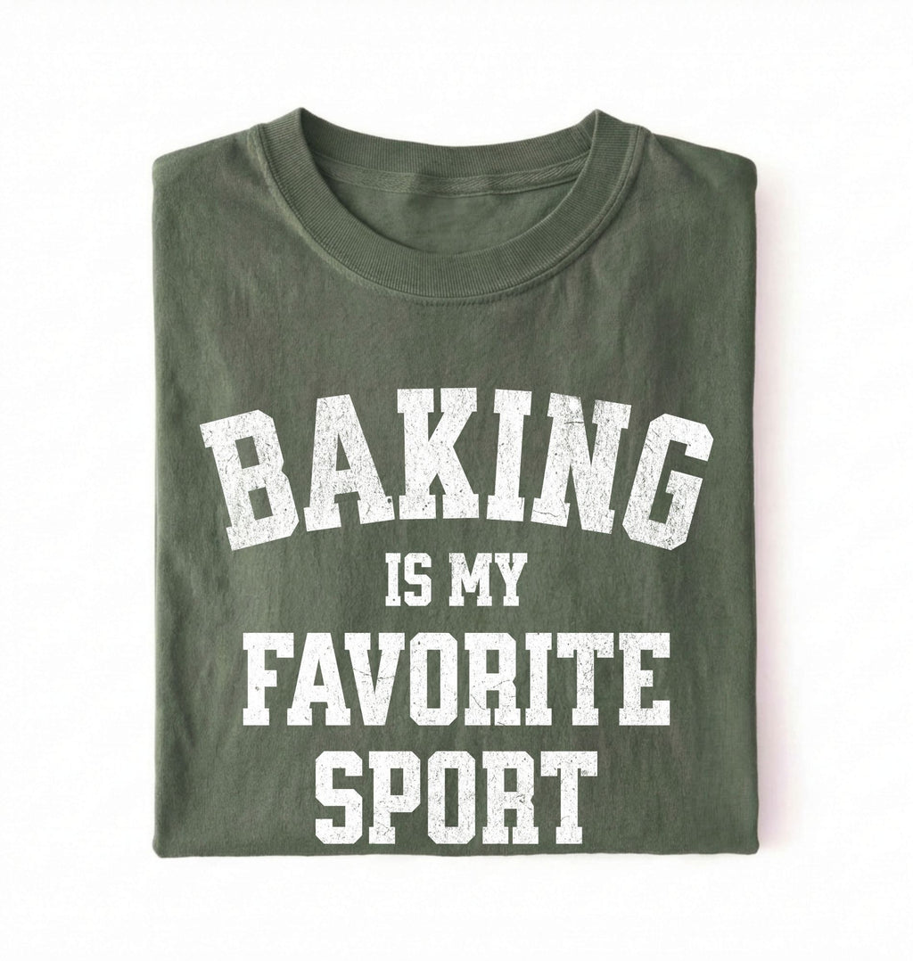 Flat lay of a green Baking Is My Favorite Sport graphic shirt on navy blue t-shirt for home bakers on a white background 