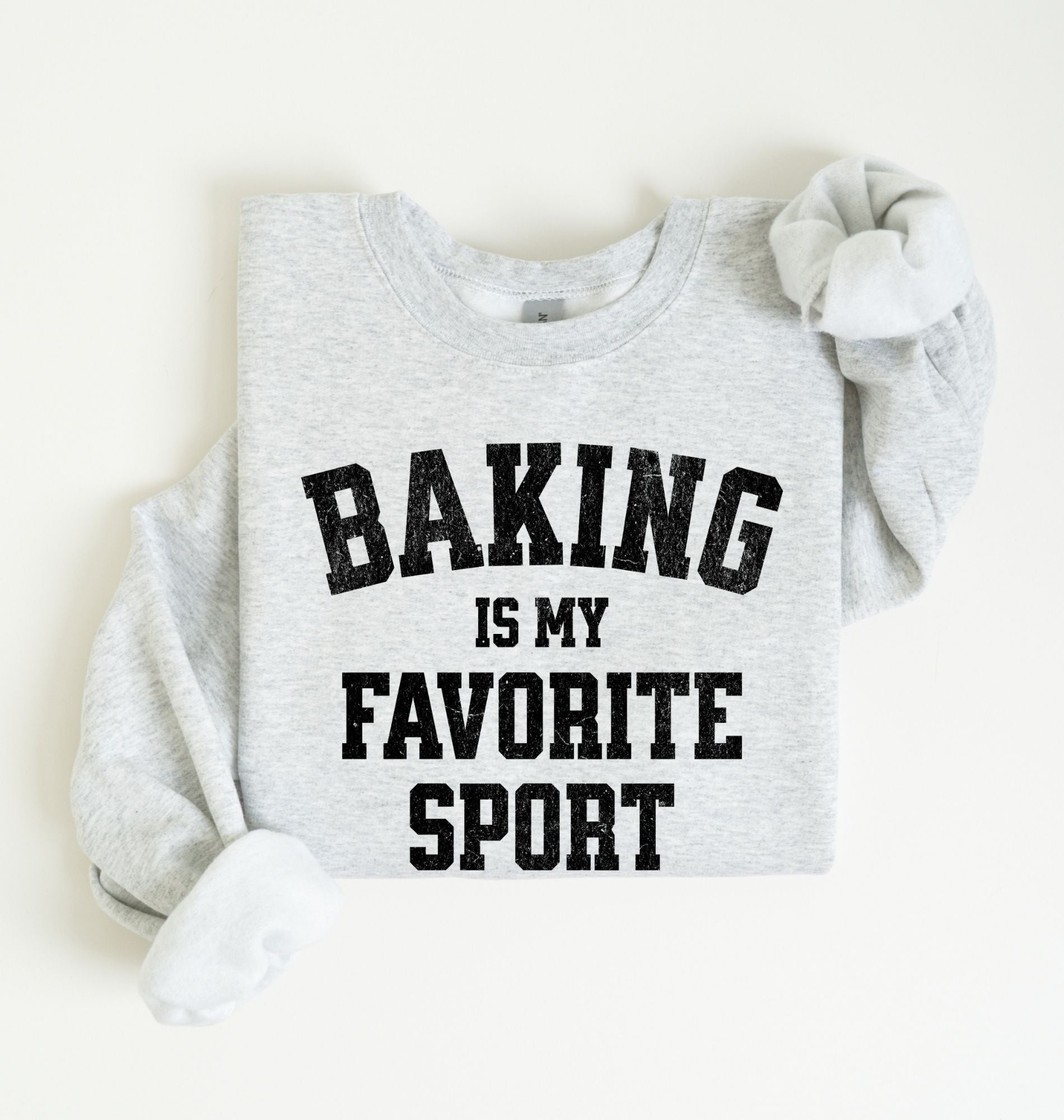 Flat lay of an ash Baking Is My Favorite Sport graphic sweatshirt on navy blue crewneck for home bakers on white background