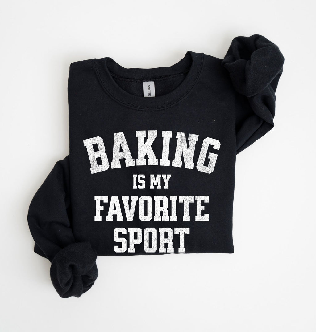Flat lay of a black Baking Is My Favorite Sport graphic sweatshirt on navy blue crewneck for home bakers on white background