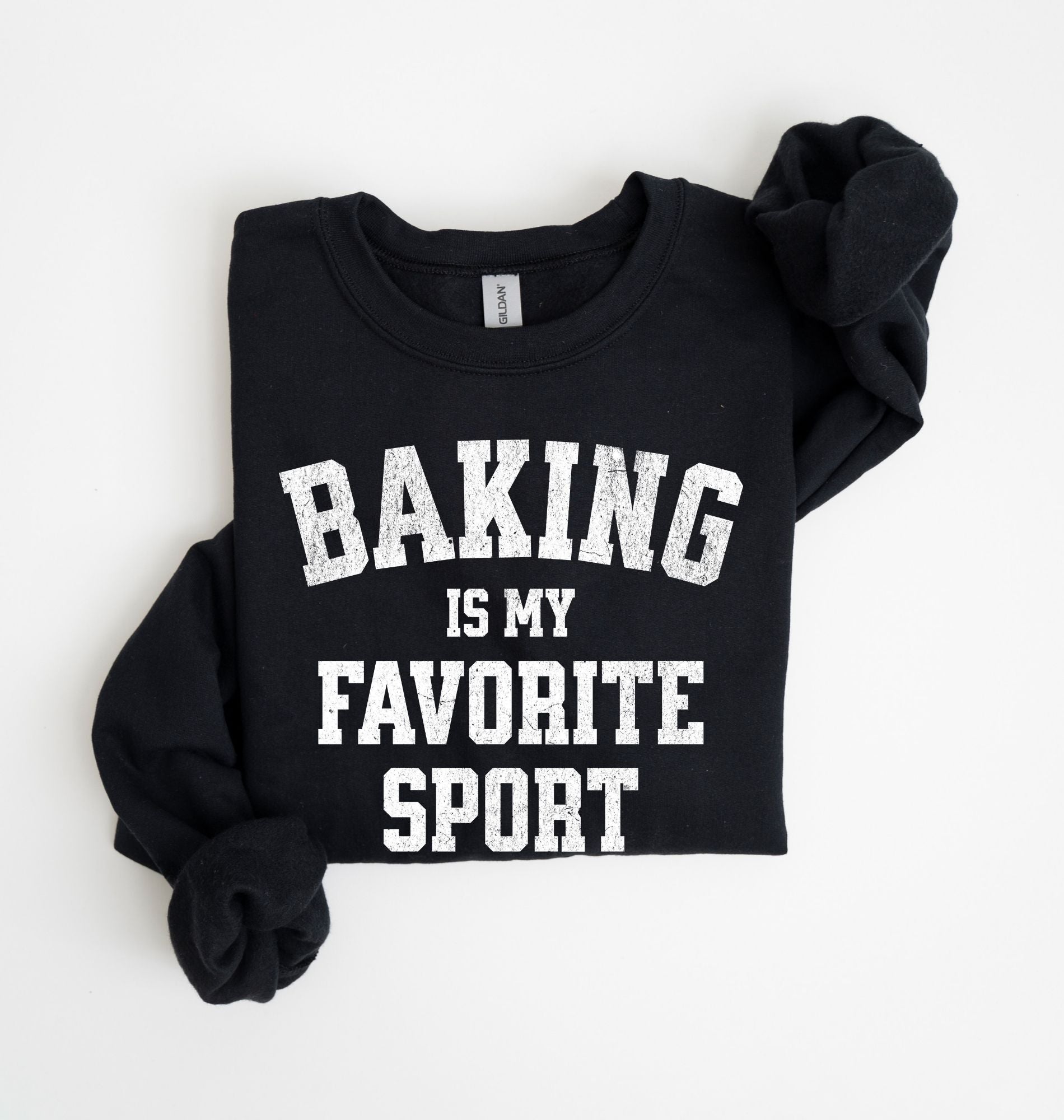 Flat lay of a black Baking Is My Favorite Sport graphic sweatshirt on navy blue crewneck for home bakers on white background