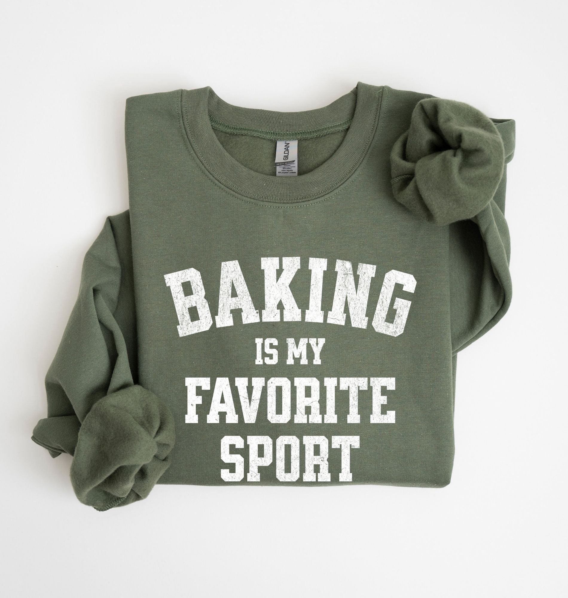 Flat lay of a green Baking Is My Favorite Sport graphic sweatshirt on navy blue crewneck for home bakers on white background