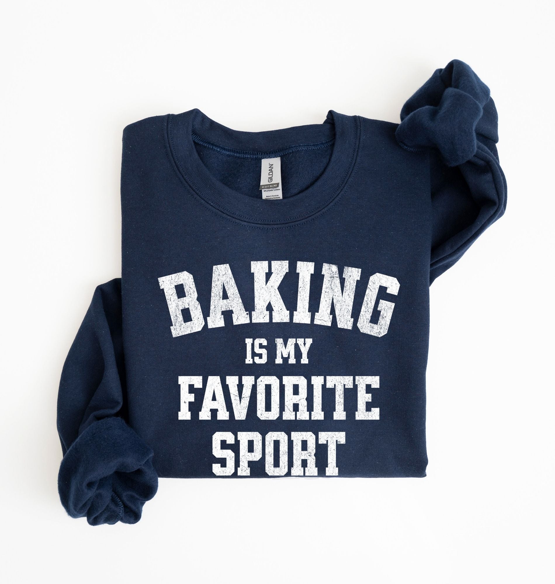 Flat lay of a navy Baking Is My Favorite Sport graphic sweatshirt on navy blue crewneck for home bakers on white background