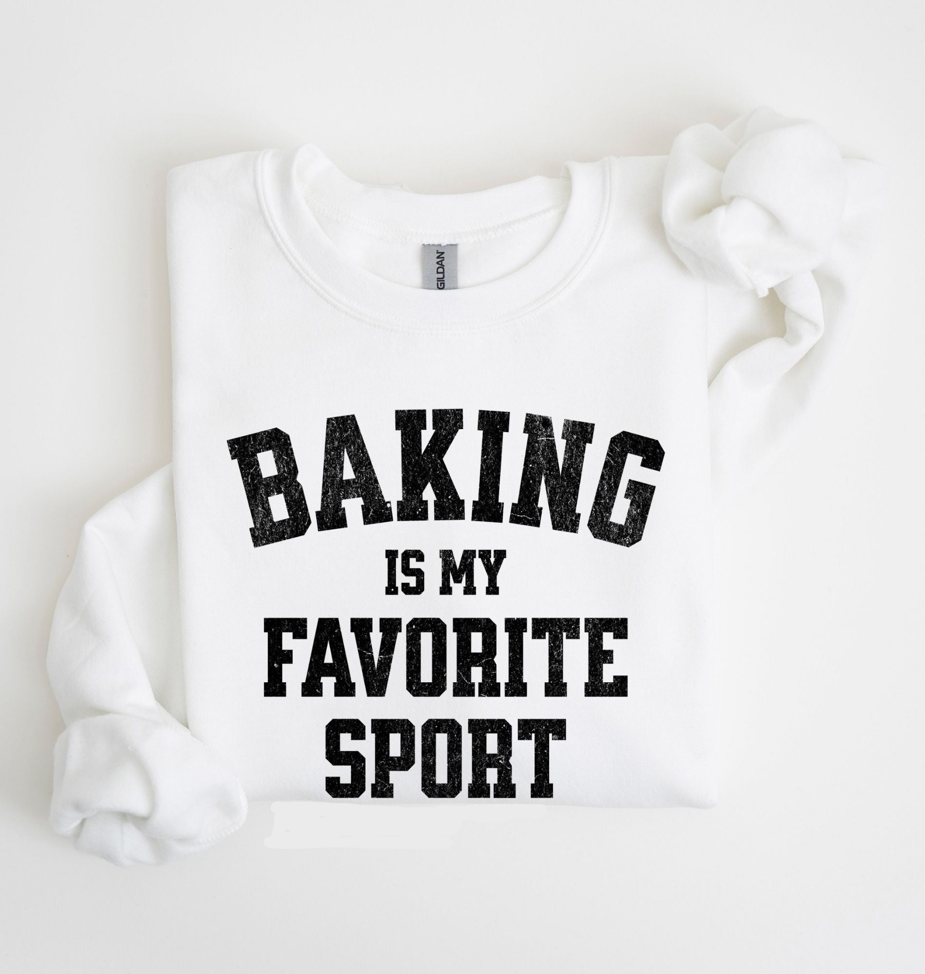 Flat lay of a white Baking Is My Favorite Sport graphic sweatshirt on navy blue crewneck for home bakers on white background