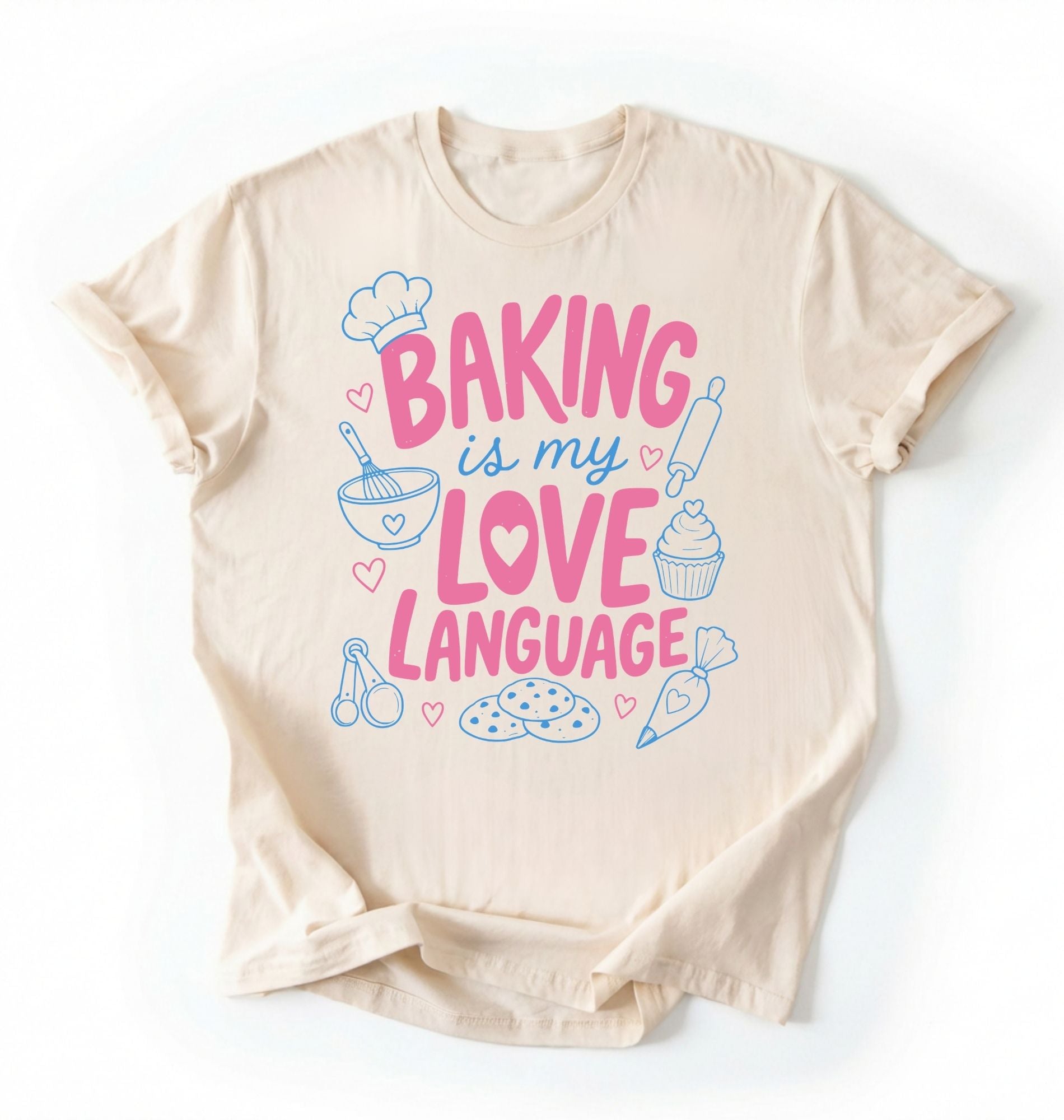 Flat lay of a Baking Is My Love Language shirt with baking tools and dessert graphics on cream t-shirt on a white background