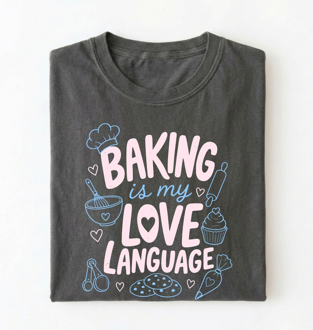 Flat lay of a Baking Is My Love Language shirt with baking tools and dessert graphics on charcoal t-shirt on a white background