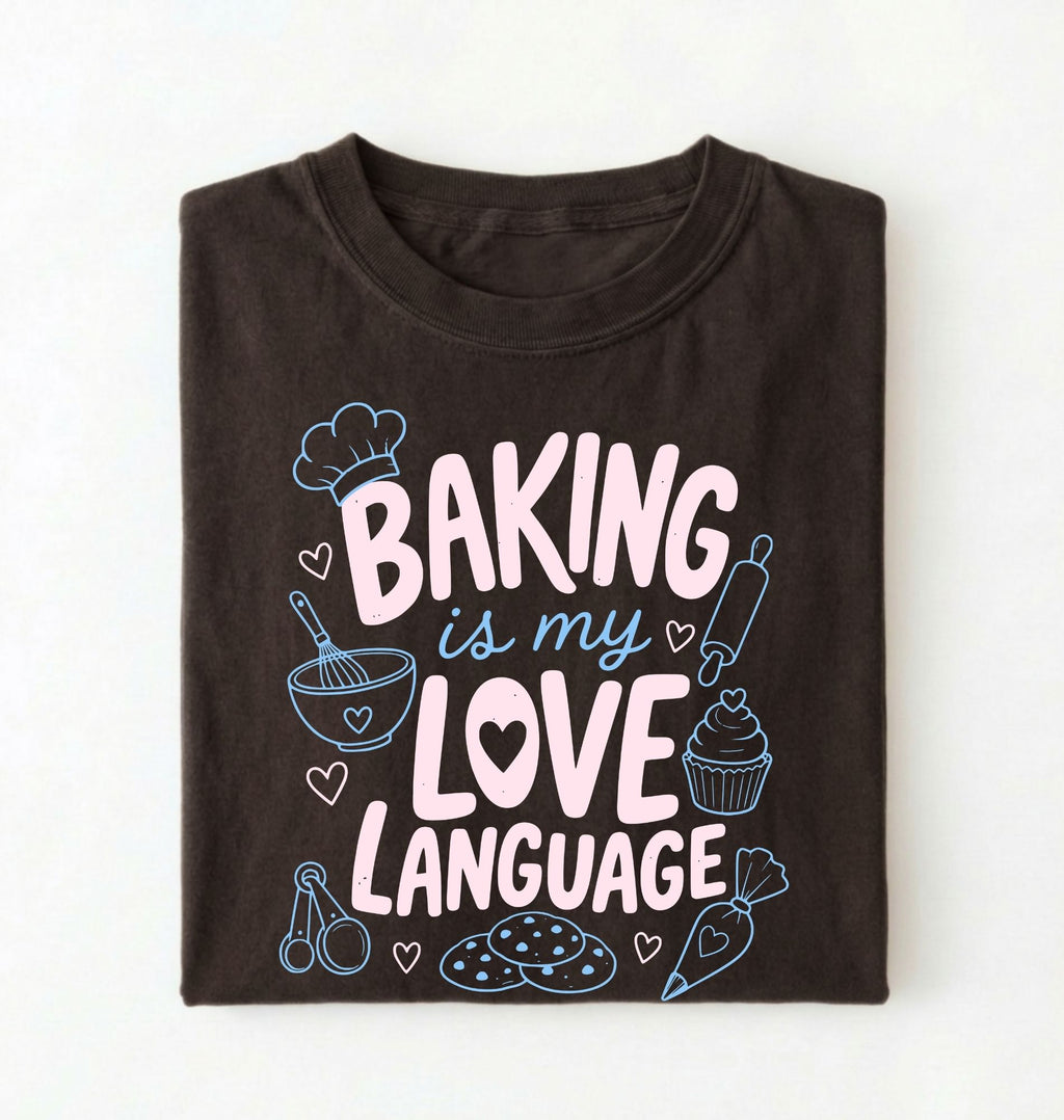 Flat lay of a Baking Is My Love Language shirt with baking tools and dessert graphics on brown t-shirt on a white background