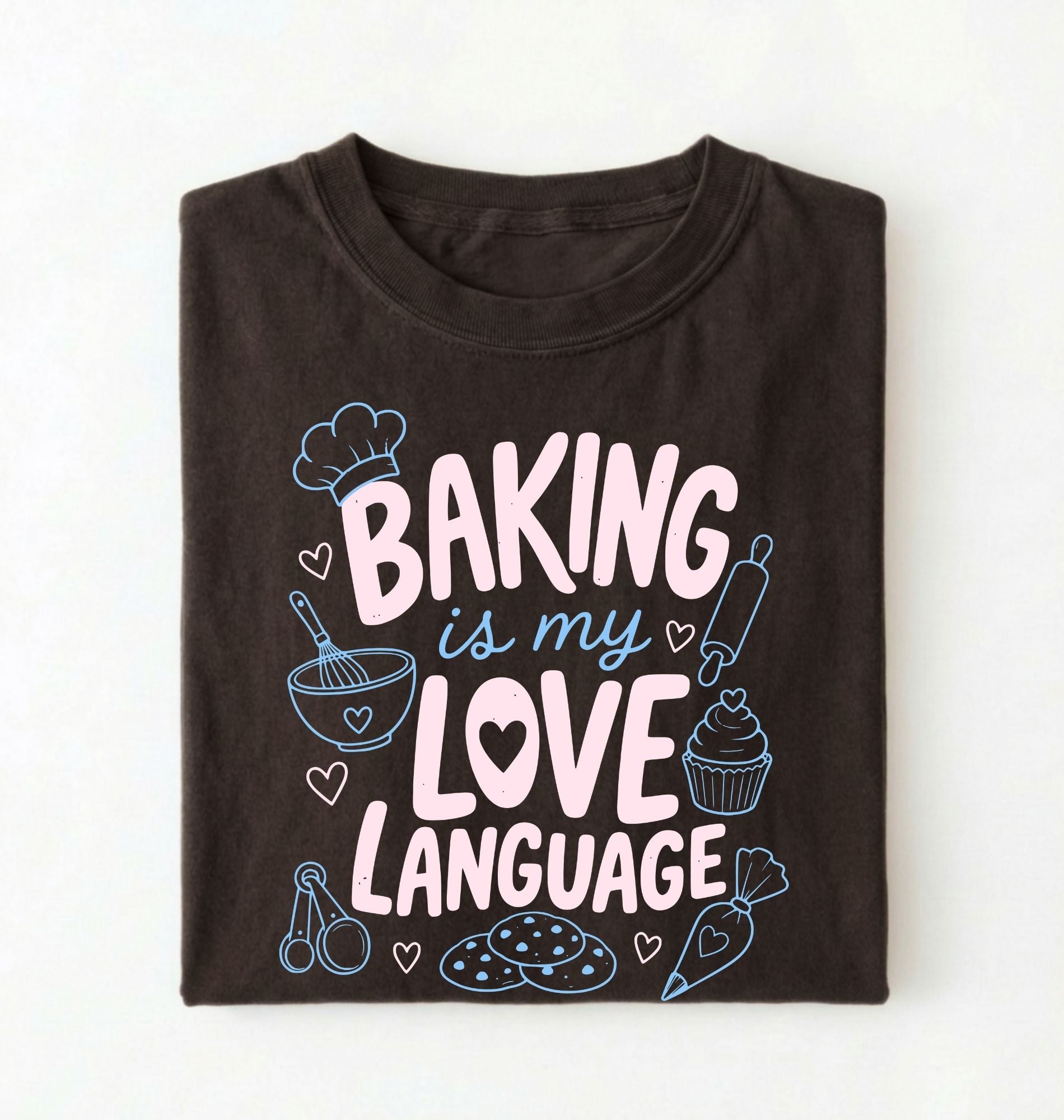 Flat lay of a Baking Is My Love Language shirt with baking tools and dessert graphics on brown t-shirt on a white background