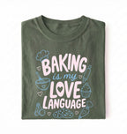 Flat lay of a Baking Is My Love Language shirt with baking tools and dessert graphics on green t-shirt on a white background