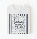 Flat lay of a white Baking Mom Club graphic shirt with baking tools and dessert icons for home bakers on a white background 