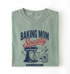 Flat lay of a bay baking mom society shirt with stand mixer and baking ingredients baking mom gift on a white background 