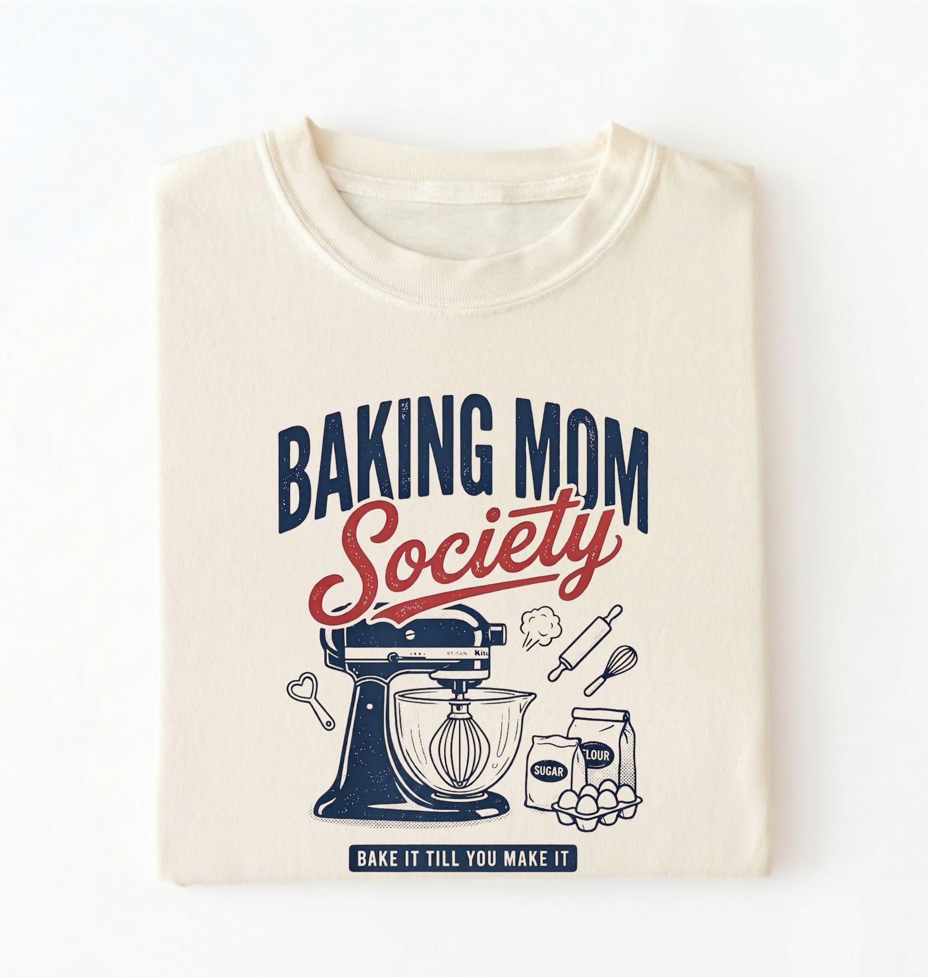 Flat lay of a cream baking mom society shirt with stand mixer and baking ingredients baking mom gift on a white background 