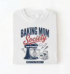 Flat lay of a white baking mom society shirt with stand mixer and baking ingredients baking mom gift on a white background 