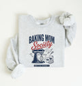 Flat lay of a ash Baking Mom Society graphic sweatshirt featuring a vintage mixer and baking tools for home bakers on a white background 