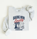 Flat lay of a ash Baking Mom Society graphic sweatshirt featuring a vintage mixer and baking tools for home bakers on a white background 