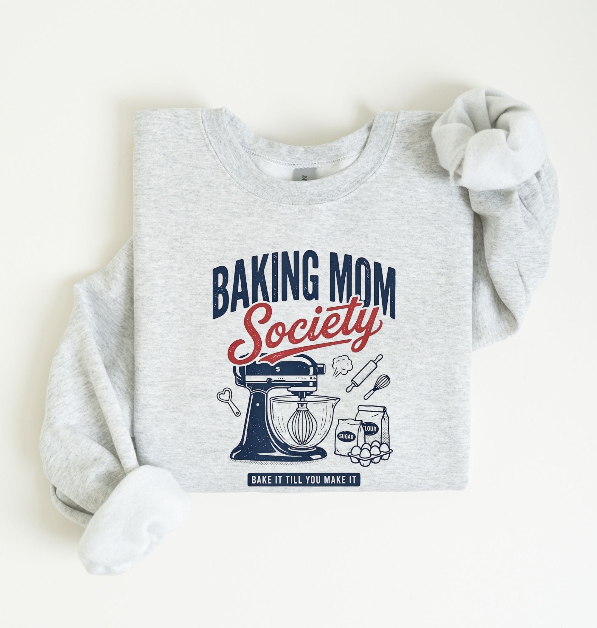 Flat lay of a ash Baking Mom Society graphic sweatshirt featuring a vintage mixer and baking tools for home bakers on a white background 