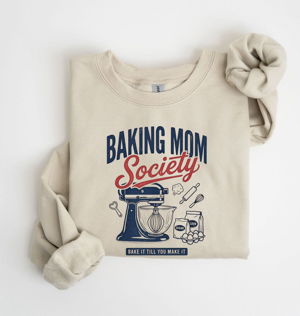 Flat lay of a sand Baking Mom Society graphic sweatshirt featuring a vintage mixer and baking tools for home bakers on a white background 