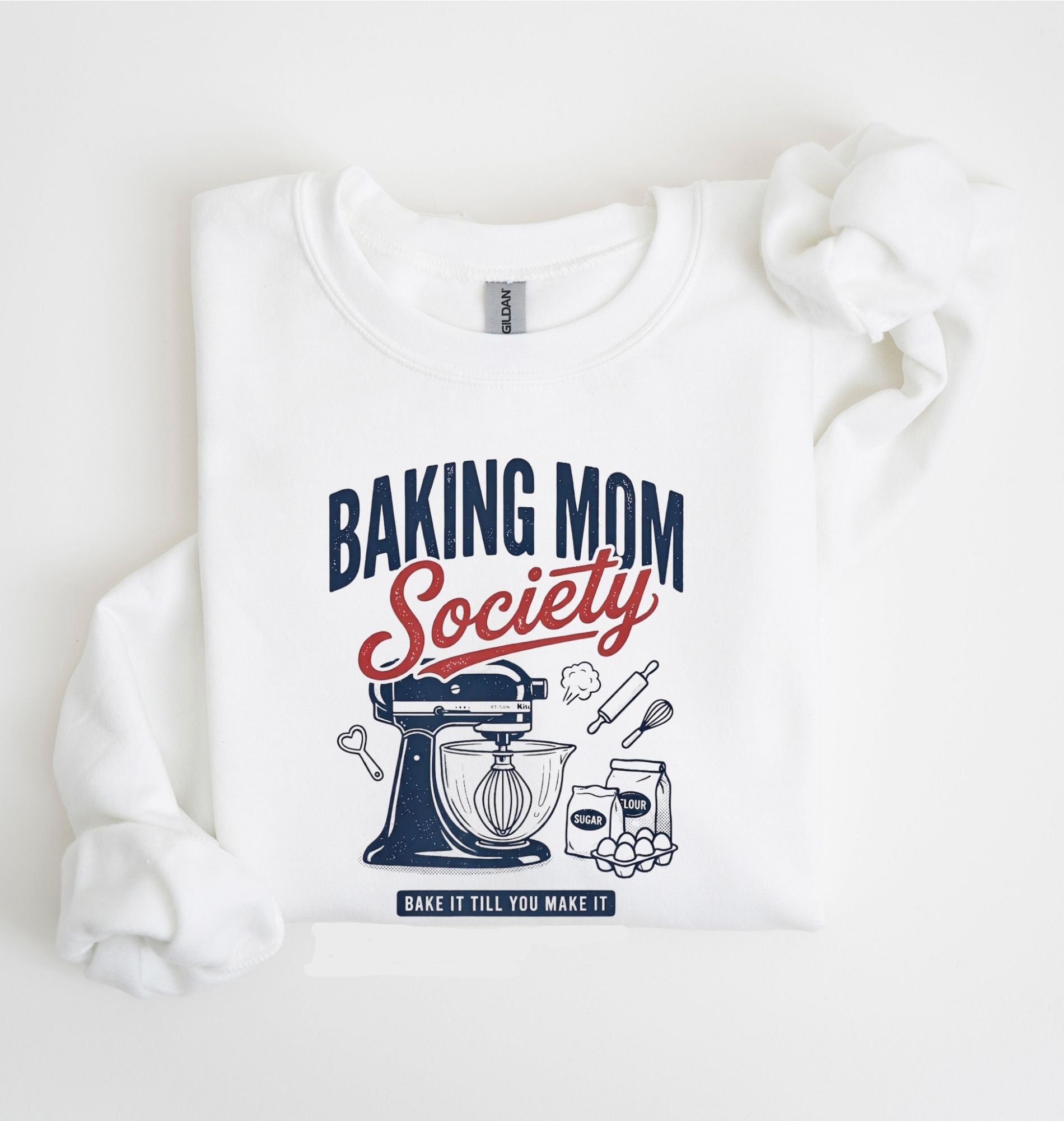 Flat lay of a white Baking Mom Society graphic sweatshirt featuring a vintage mixer and baking tools for home bakers on a white background 