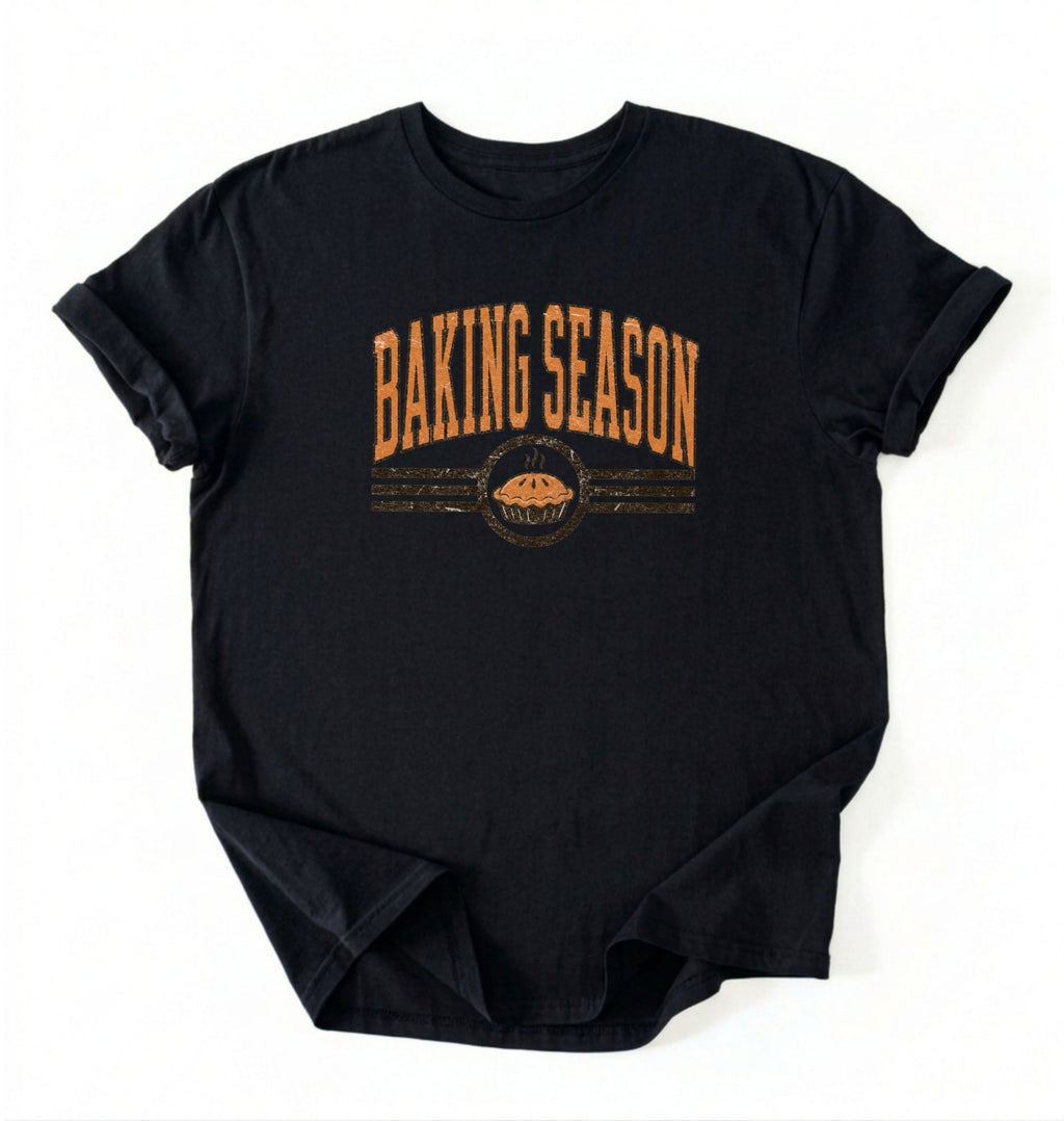 A black short-sleeve t-shirt with a distressed orange graphic that reads 'BAKING SEASON' above a pie illustration, laid flat on a white background.