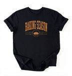 A black short-sleeve t-shirt with a distressed orange graphic that reads 'BAKING SEASON' above a pie illustration, laid flat on a white background.