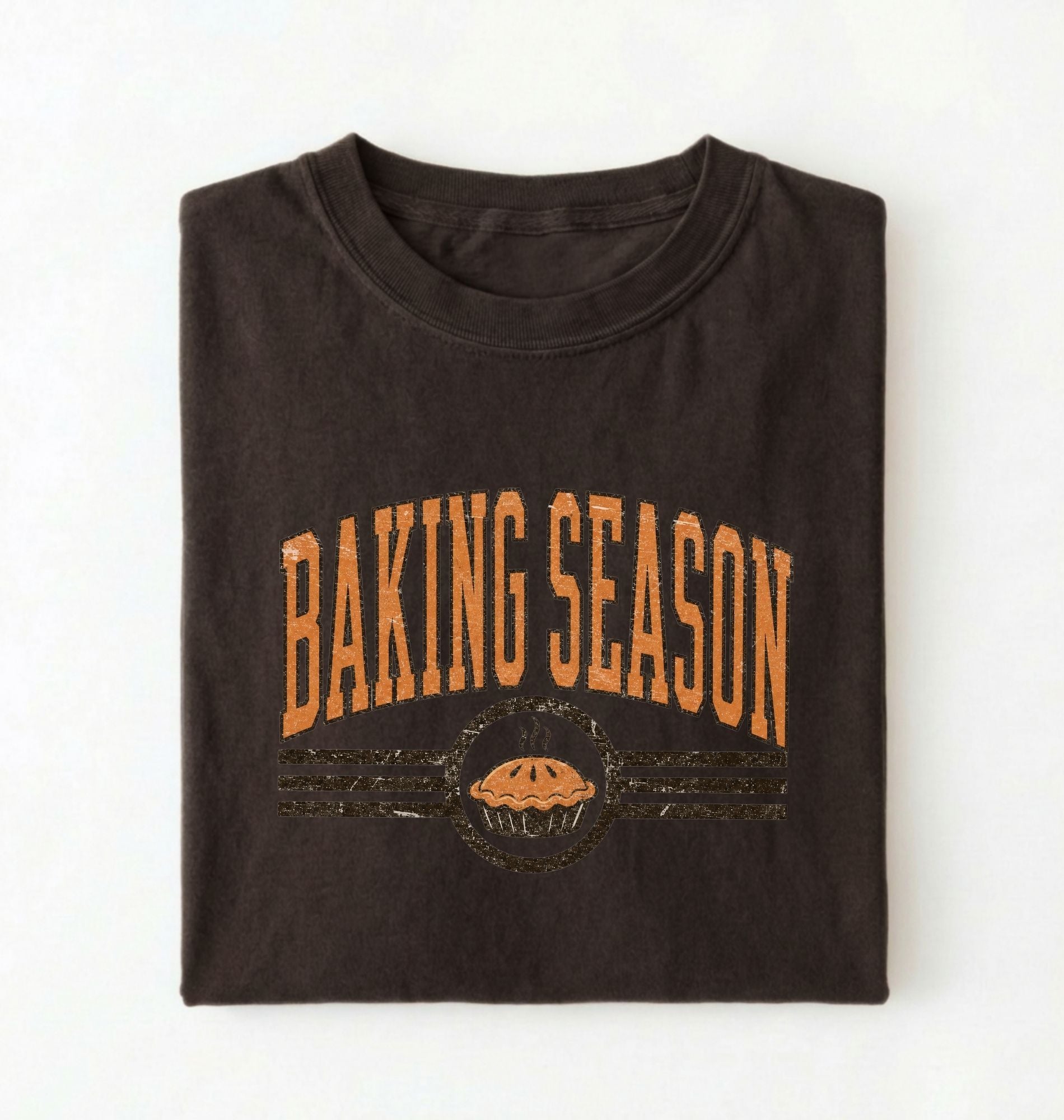 A dark brown folded t-shirt with a distressed orange graphic that reads 'BAKING SEASON' above a pie illustration, displayed on a clean white background.